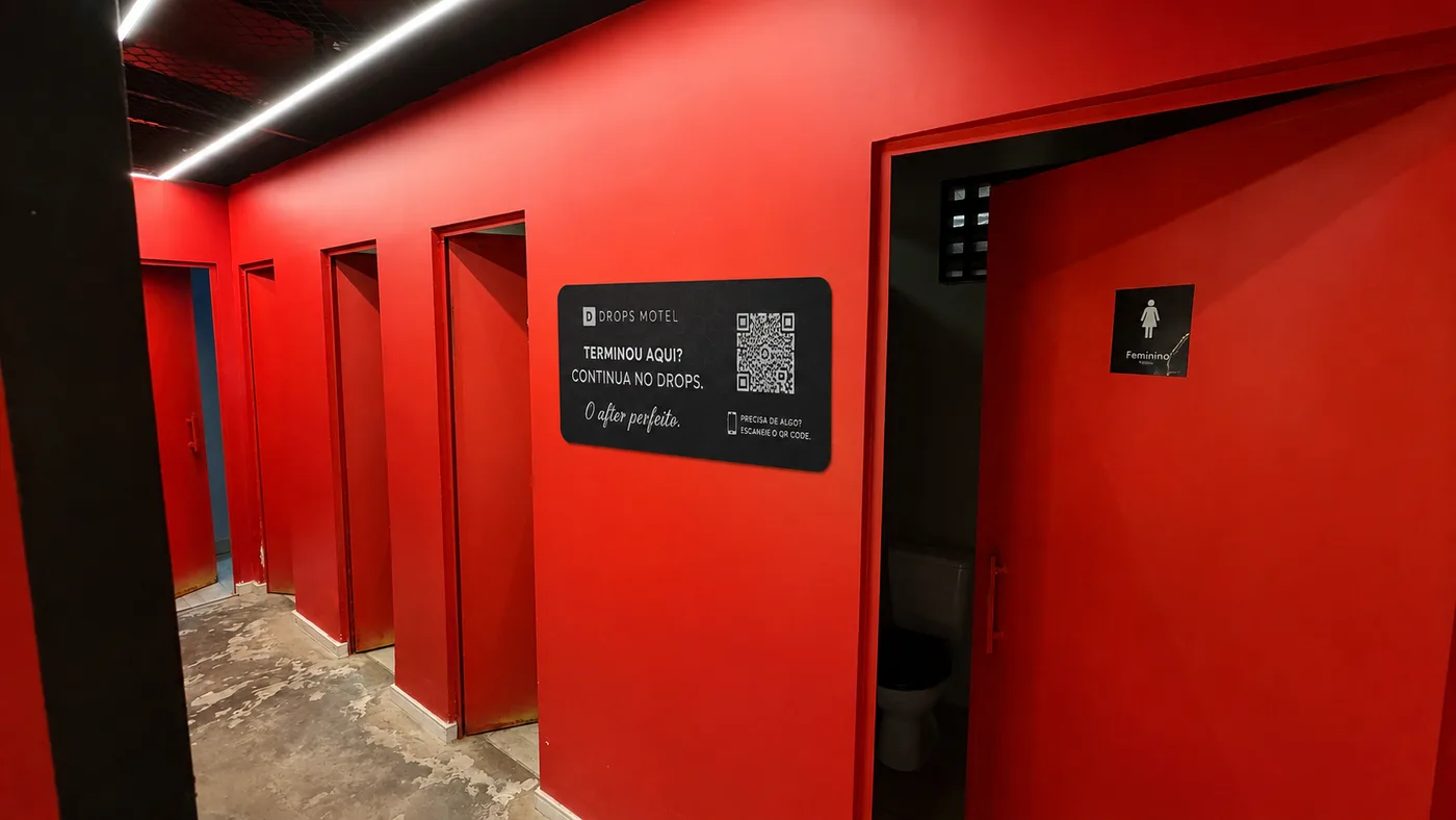 Placa da ação Drops Motel instalada no corredor vermelho de um bar